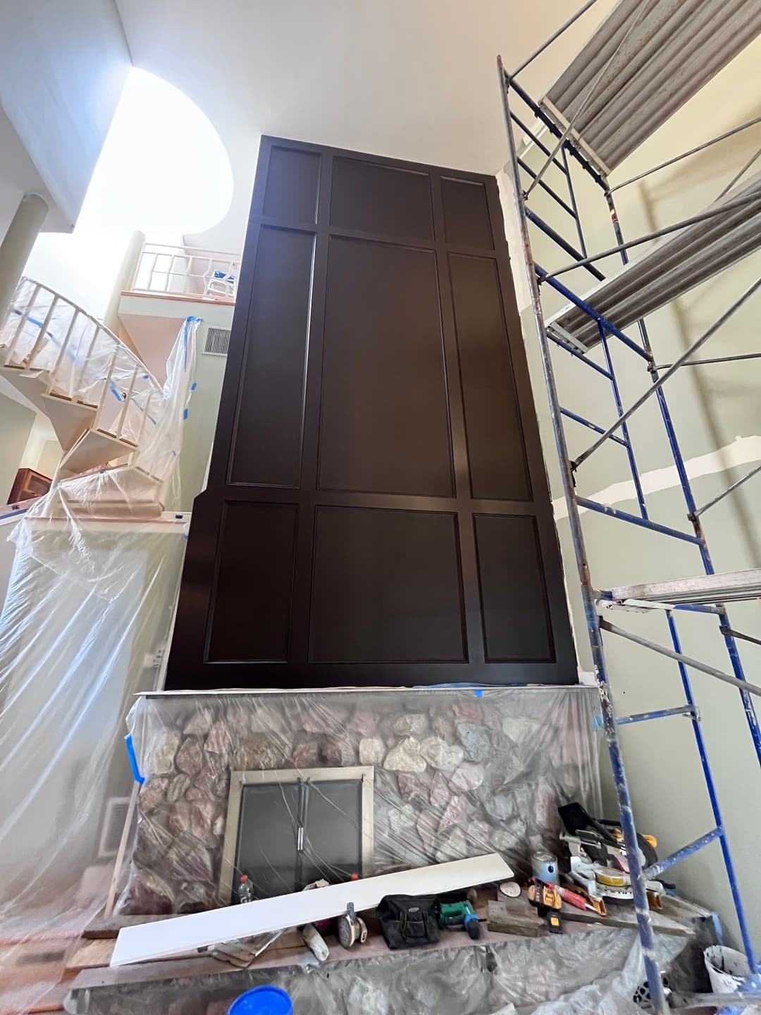 Modern home interior featuring a tall, dark paneled wall under construction with tools and scaffolding.