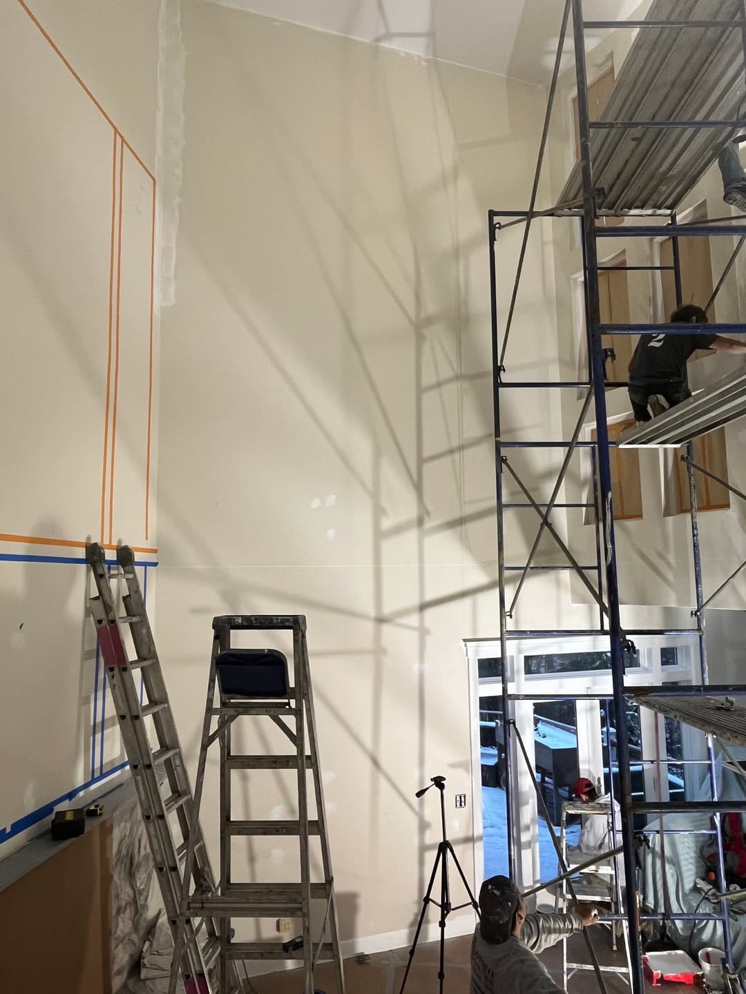 Interior painting project with scaffolding and ladders, showcasing wall preparation and shadows.