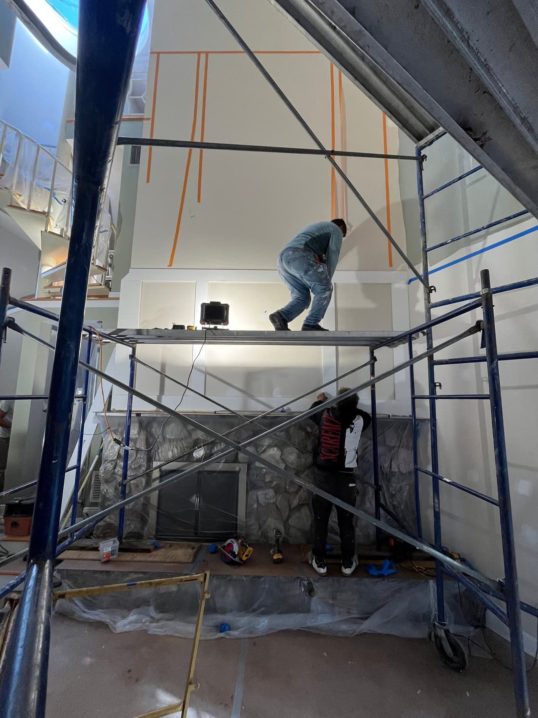 Workers installing drywall on a tall wall using scaffolding in a home renovation project.
