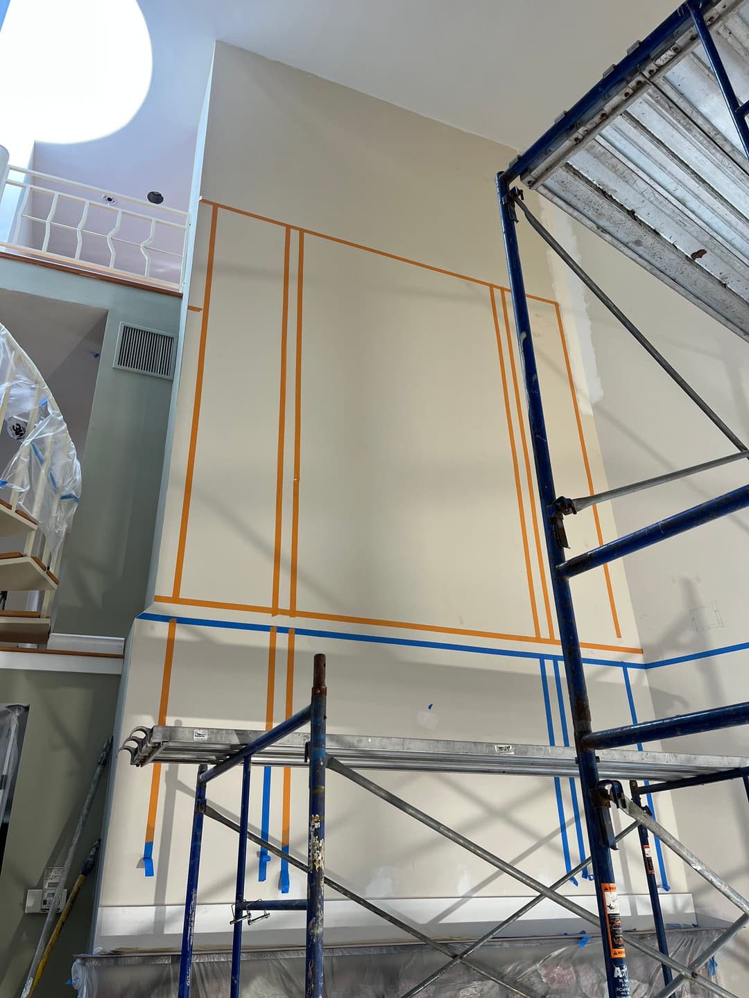 Interior painting preparation with painter's tape on walls, scaffolding setup in a home.