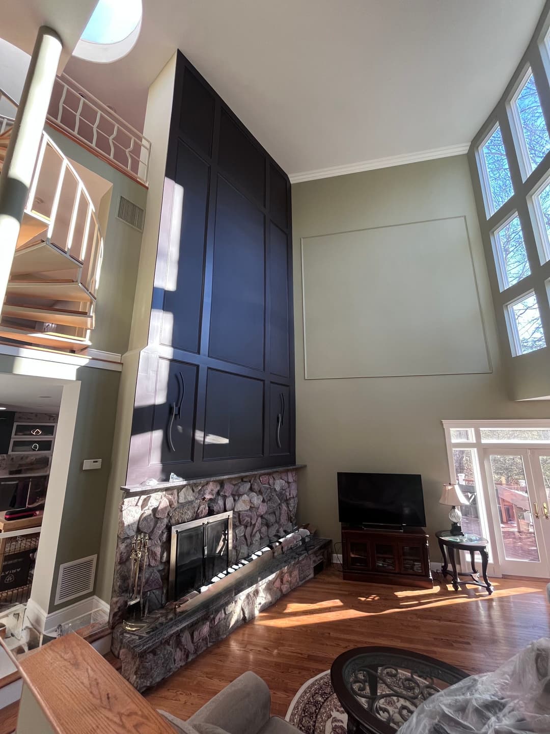 Modern living room with a tall dark wood feature wall, stone fireplace, and large windows.