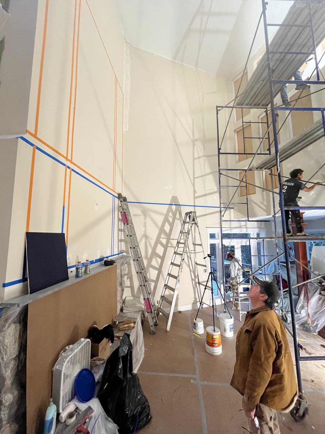 Interior painting project with scaffolding, ladders, and workers preparing walls.