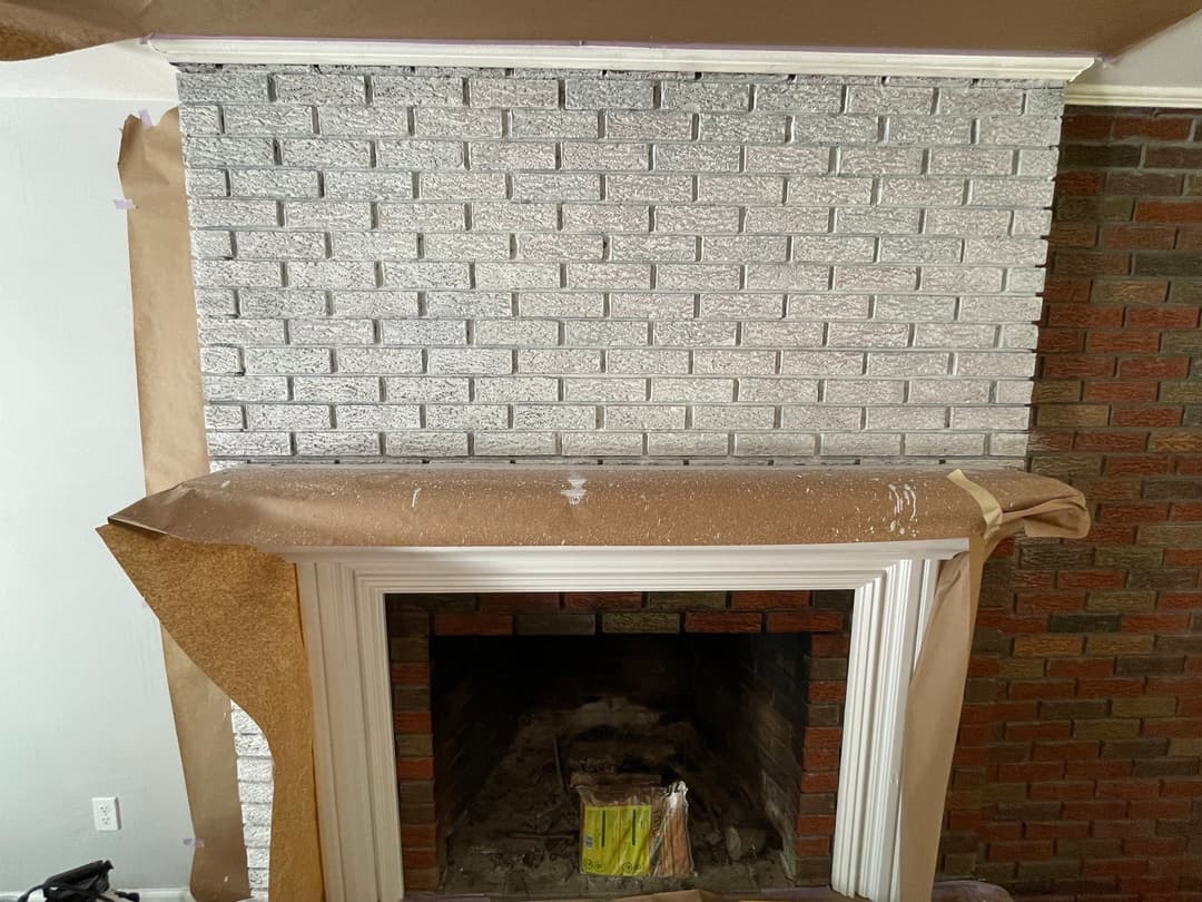 Partial view of a fireplace with a newly painted silver brick wall and protective cover.