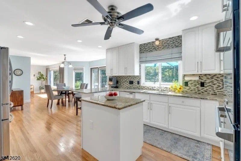 Modern kitchen with white cabinets, granite island, ceiling fan, and natural light.