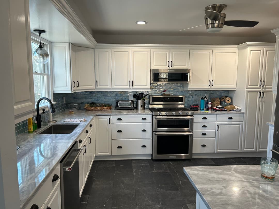 Modern white kitchen with stainless steel appliances, marble countertops, and black tile flooring.