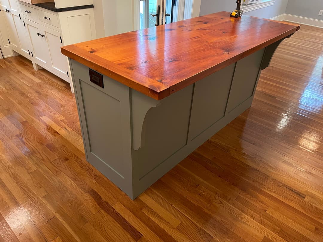 Kitchen island with a rustic wood top and light green base, surrounded by hardwood flooring.