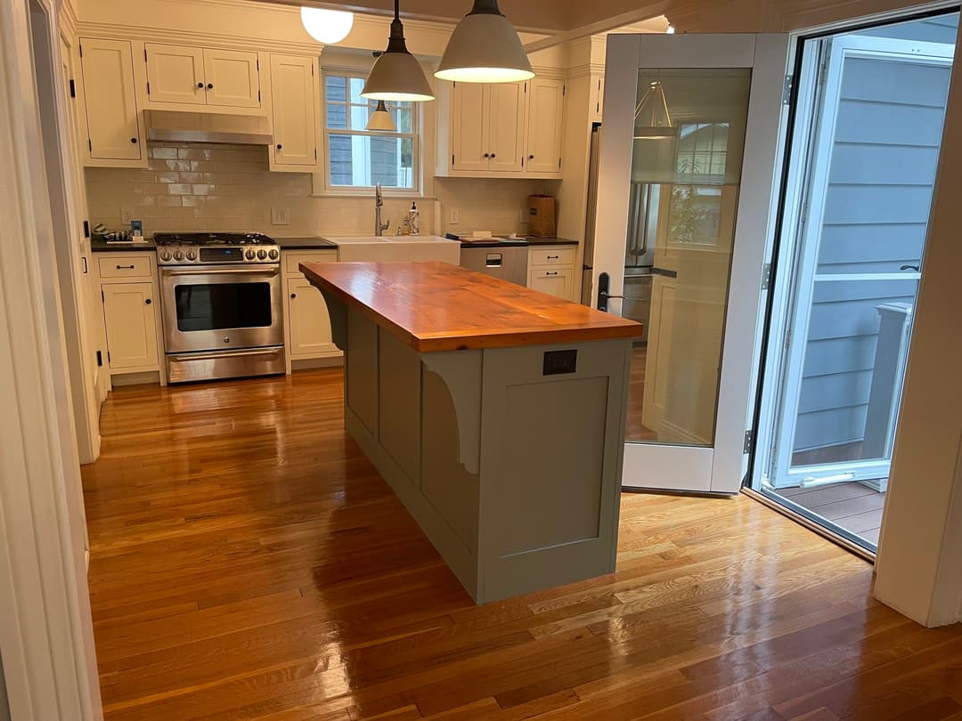 Modern kitchen interior with wooden island, stainless steel appliances, and open door to outdoor space.