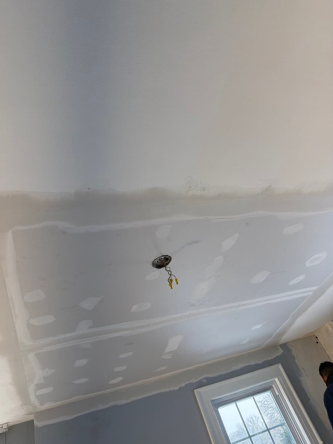 Newly finished drywall ceiling with visible patches and lighting fixture in a room.