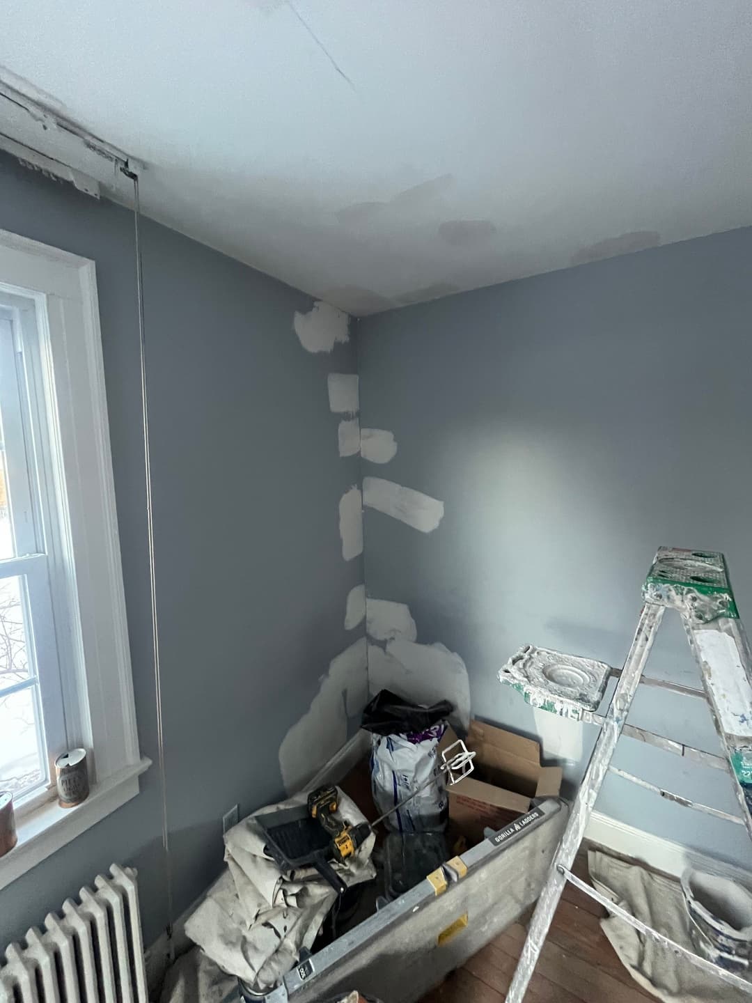 Room undergoing renovation with gray walls, ladder, and painting supplies.