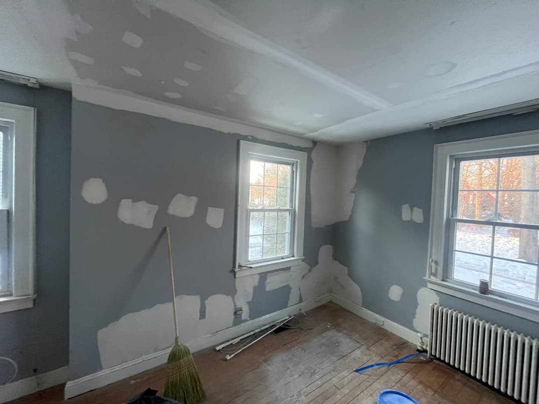 Renovation of a room with gray walls, unpainted patches, wooden floor, and two windows.